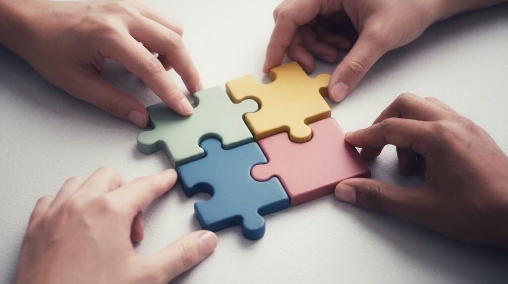 Four people join colorful puzzle pieces together on a table.